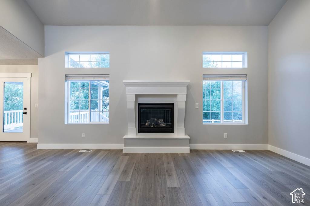 Spacious room featuring a central fireplace with a white mantel and surround, wood-finish flooring, white baseboards, and multiple windows