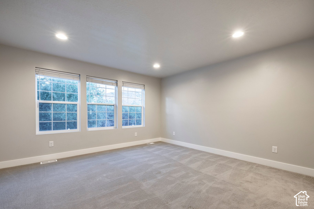 Spacious room featuring three large windows, recessed ceiling lights, light gray carpet, and neutral wall tones