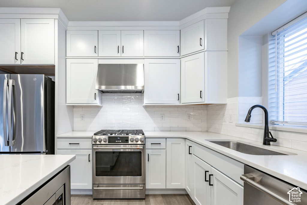 Kitchen featuring white shaker cabinetry, stainless steel appliances, white subway tile backsplash, and light-toned countertops