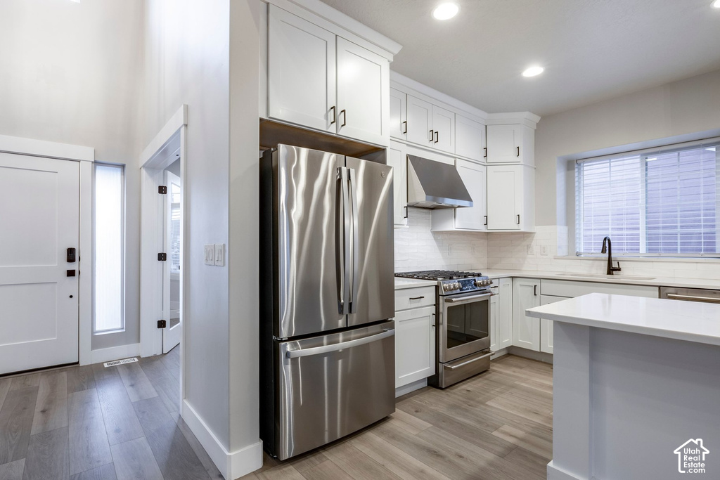 Modern kitchen featuring white cabinetry, stainless steel appliances, light countertops, wood-finish flooring, and recessed lighting