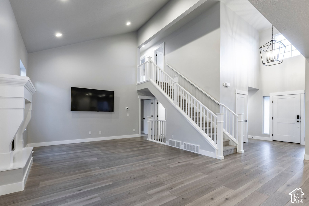 Spacious living area featuring high vaulted ceilings, light wood-finish flooring, a white mantel, and a dual-level staircase with white railings