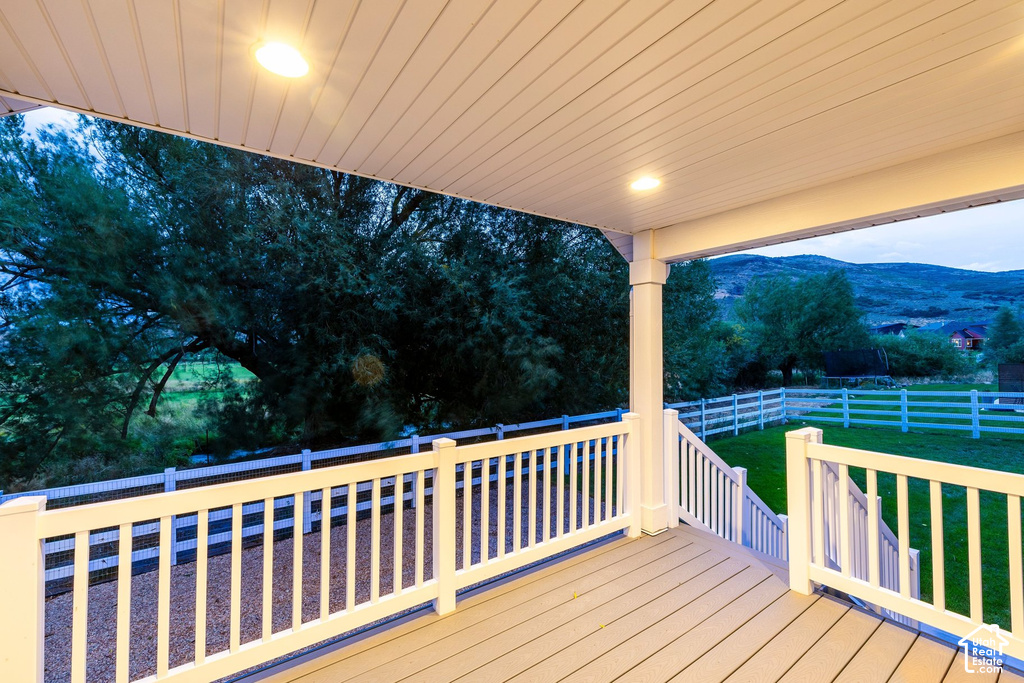 Covered porch with recessed lighting, composite decking, white balusters, and a mountain backdrop