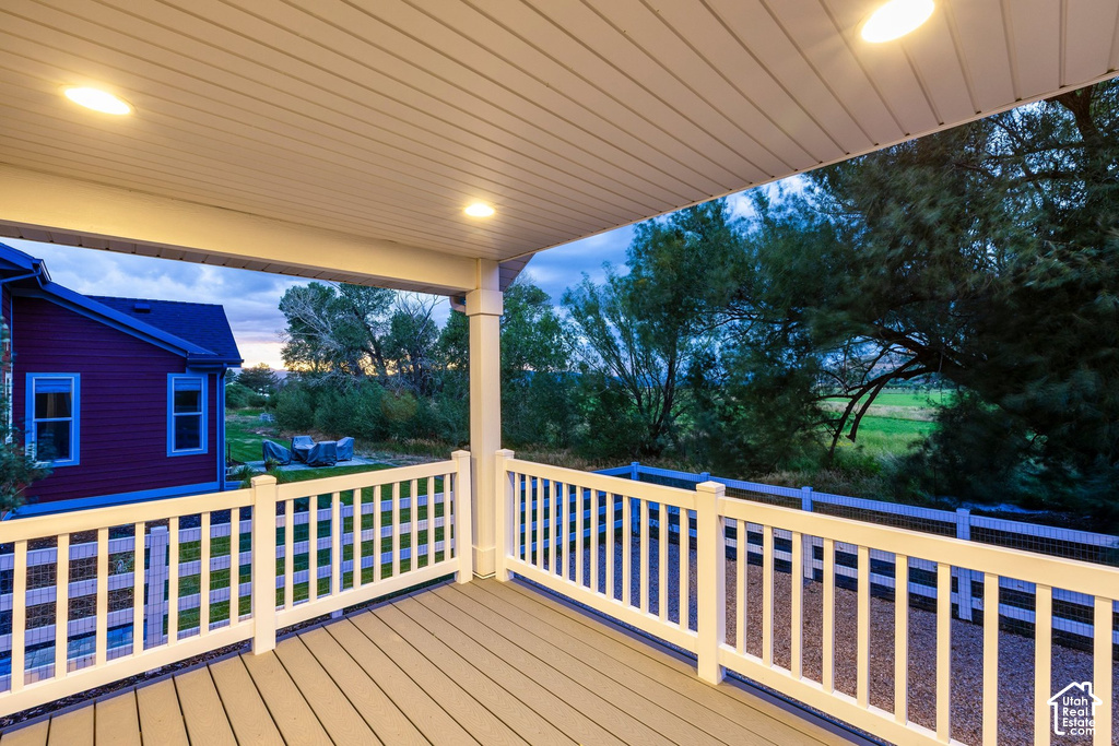 Covered outdoor deck featuring composite decking, white railing, recessed lighting, and a distant field