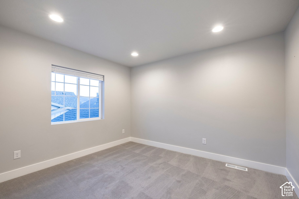 Neutral wall paint, recessed ceiling lighting, a grid-pattern window with blinds, plush gray carpet, and white baseboards