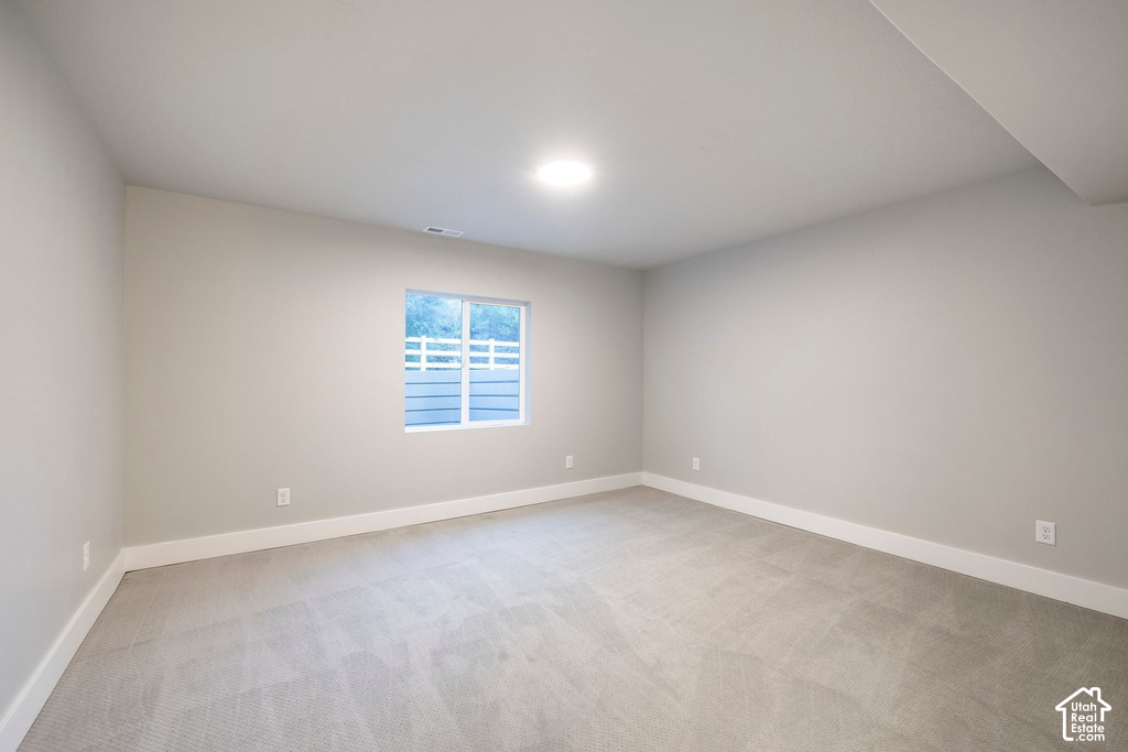 Spacious room featuring light gray carpeting, neutral-toned walls, a white-framed window, recessed lighting, and white baseboards