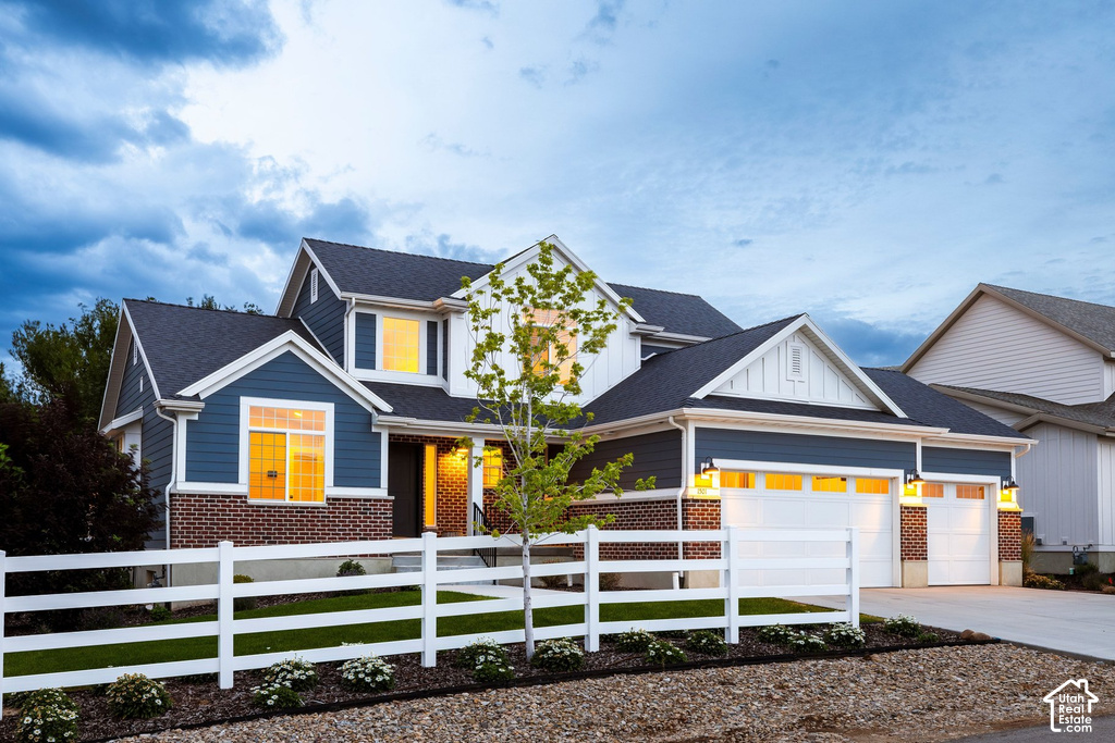 Multi-level residence featuring a blue and white siding exterior with brick accents, white fencing, and a two-car garage