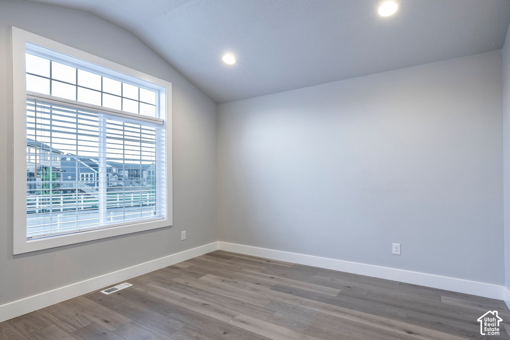 Bright and airy bedroom featuring a large multi-pane window with plantation shutters, recessed lighting, wood-finish flooring, and fresh neutral wall finishes