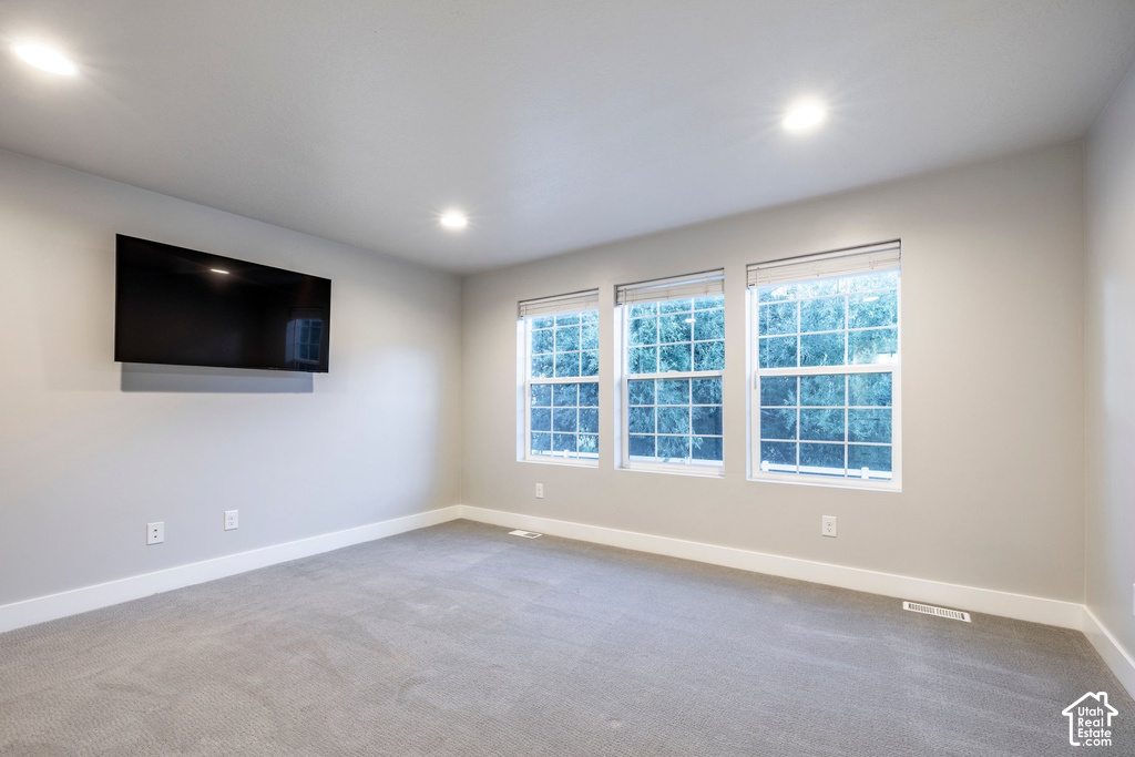 Spacious room featuring light gray walls, plush gray carpeting, and recessed lighting