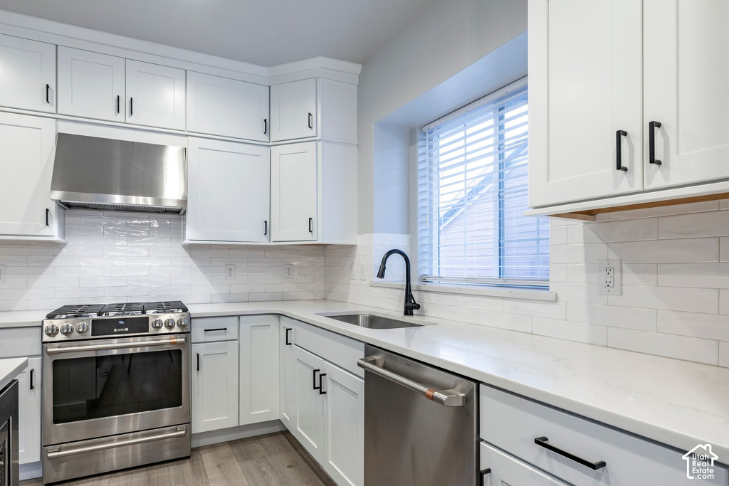 Modern kitchen featuring white shaker cabinetry, stainless steel appliances, light-toned countertops, a subway tile backsplash, and wood-finish flooring