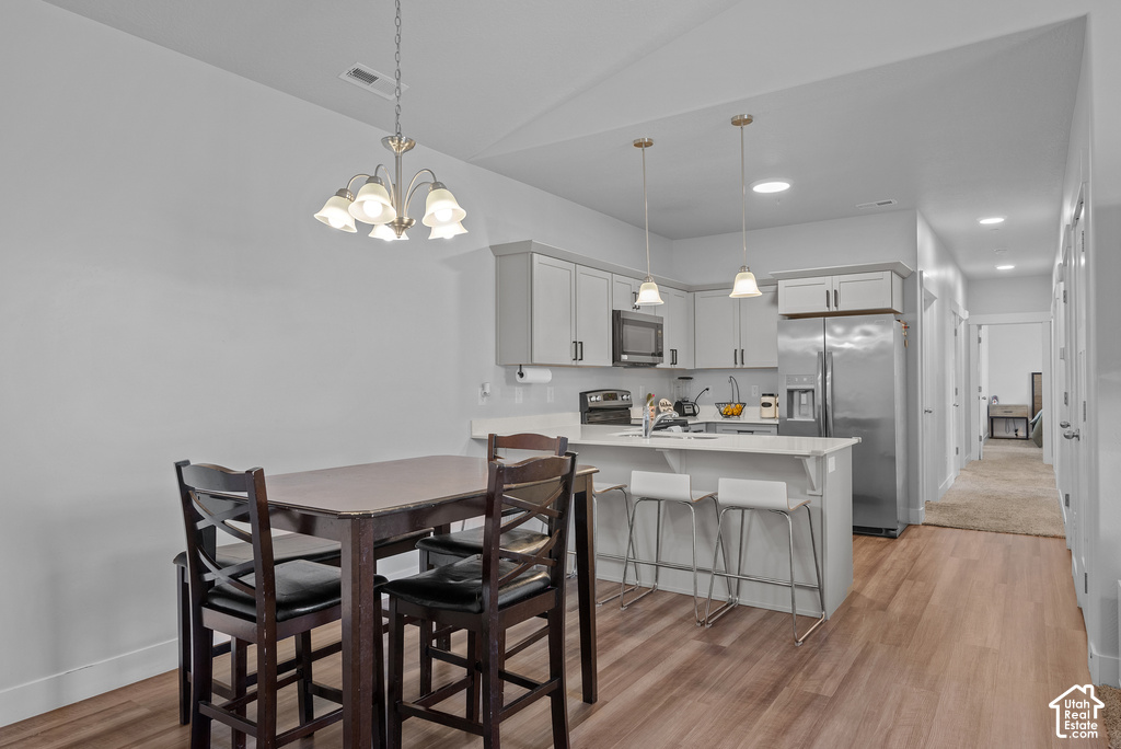 Open-concept kitchen and dining area featuring stainless steel appliances, white cabinetry with hardware accents, a kitchen island with seating, pendant lighting, and wood-finish flooring throughout