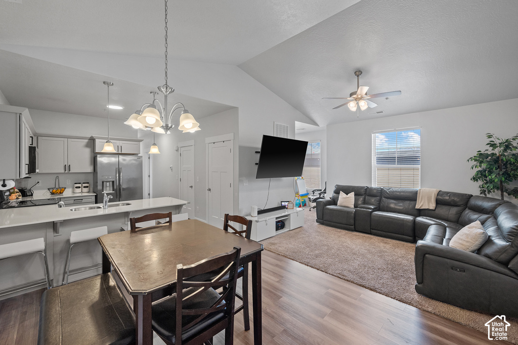 Open-concept living area featuring vaulted ceilings, wood-finish flooring, a contemporary kitchen with light-toned cabinetry and stainless steel appliances, and a dining area with a chandelier