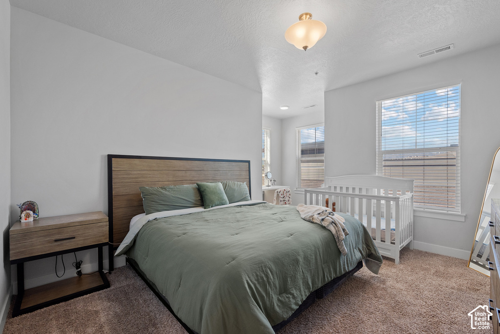 Spacious bedroom featuring a wood-frame bed with upholstered headboard, wood-finish nightstand with integrated shelving, soft-close drawers, and warm-toned carpet flooring