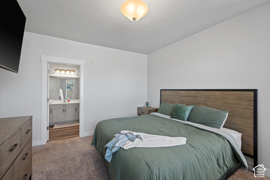 Spacious primary bedroom featuring a wood-finish platform bed with upholstered headboard, soft-close dresser with natural wood tones, plush carpeting, and an ensuite bathroom with dual vanity and abundant storage