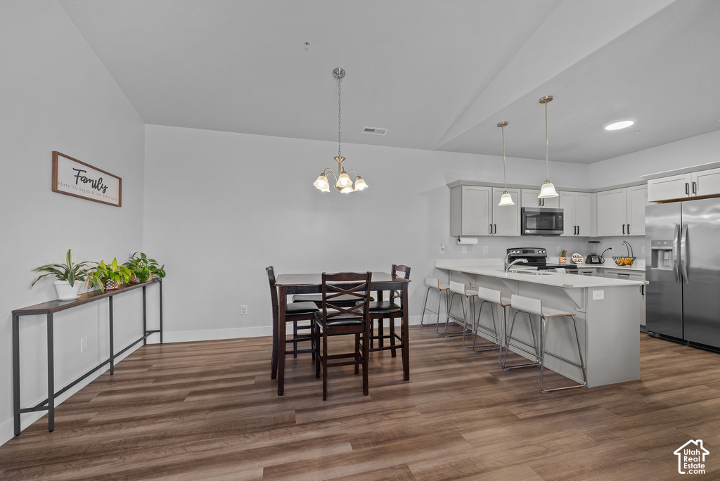 Open-concept kitchen and dining area featuring stainless steel appliances, white cabinetry with hardware accents, quartz countertops, a central island with seating, pendant lighting, wood-finish flooring throughout, and a spacious layout with high ceiling