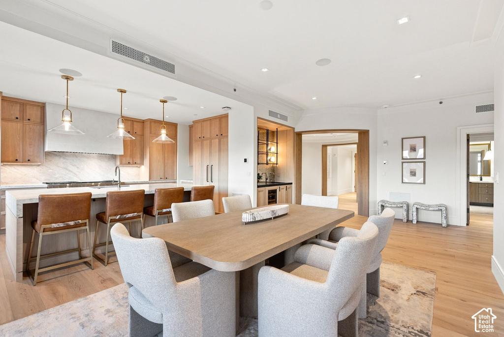 Open-concept dining and kitchen featuring a wood-top dining table with seating for six, natural wood cabinetry, stainless steel appliances, white subway tile backsplash, pendant lighting, hardwood flooring throughout, and abundant recessed ceiling lightin