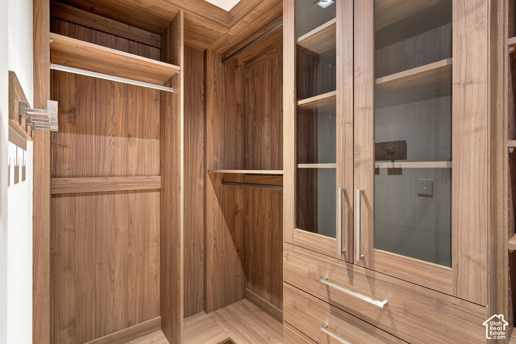 Elegant walk-in closet featuring rich wood cabinetry with glass-front upper storage, multiple shelving units, and polished chrome hardware