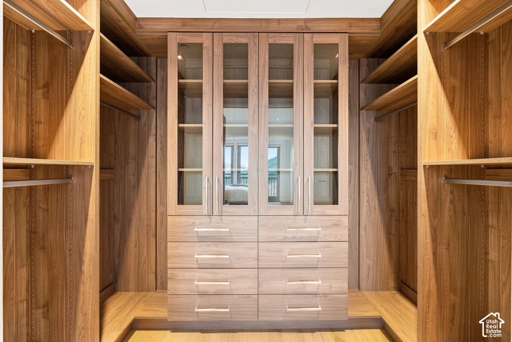 Custom wood-finish cabinetry featuring glass-front doors, built-in drawers, open shelving, and hanging rods