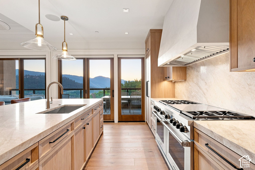 Chef's kitchen featuring light wood cabinetry, white quartz countertops, a six-burner gas range with matching hood, a large center island with prep sink, and pendant lighting