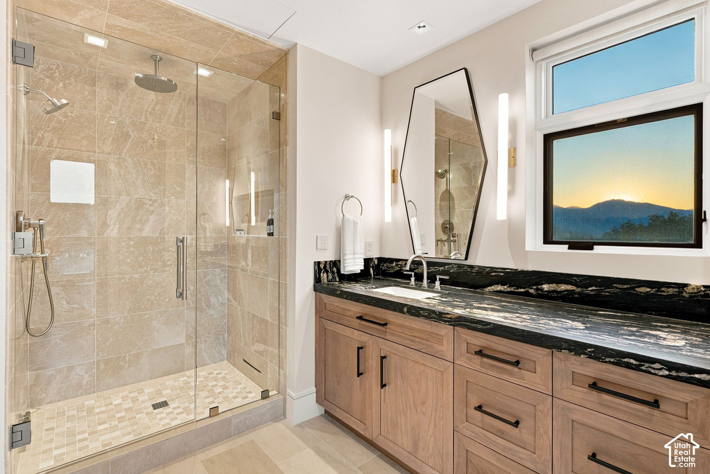 Spacious bathroom featuring a glass-enclosed shower with multiple showerheads, a long vanity with wood cabinetry, a dark stone countertop, a rectangular mirror, and sconce lighting
