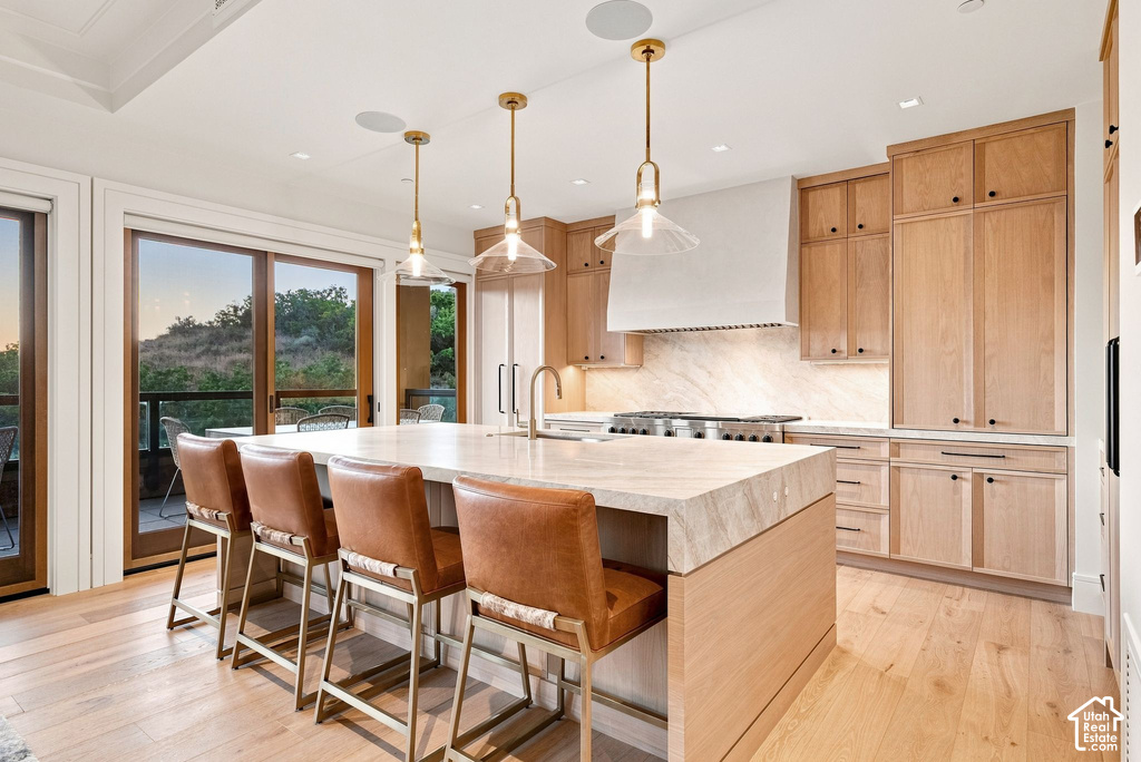 Chef's kitchen featuring natural wood cabinetry with soft-close doors, a large waterfall-edge island with seating for multiple guests, stainless steel gas cooktop, white subway tile backsplash, and quartz countertops