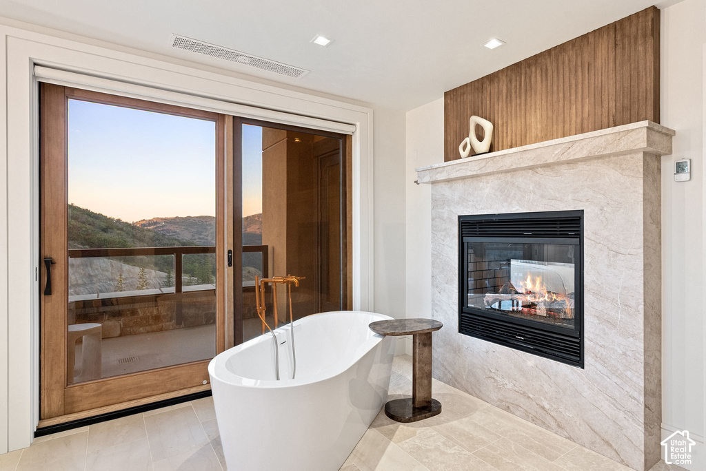 Freestanding soaking tub with a floor-mounted faucet, set against a modern fireplace with a light-toned stone surround and a rich wood accent panel
