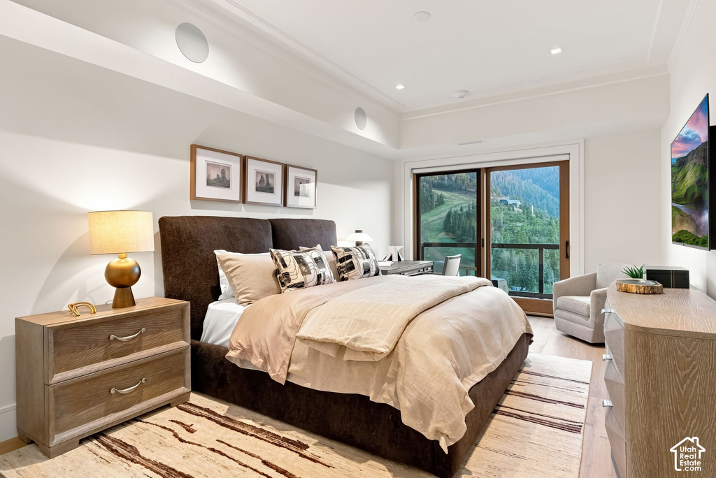Spacious bedroom featuring wood-finish flooring, a full-height glass sliding door, crown molding, integrated ceiling speakers, and recessed lighting