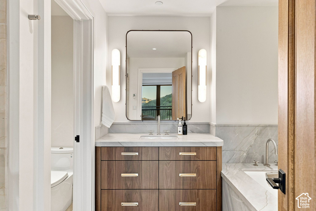 Bathroom vanity featuring a wood-finish cabinet with gold-toned hardware, a white countertop, and an undermount sink