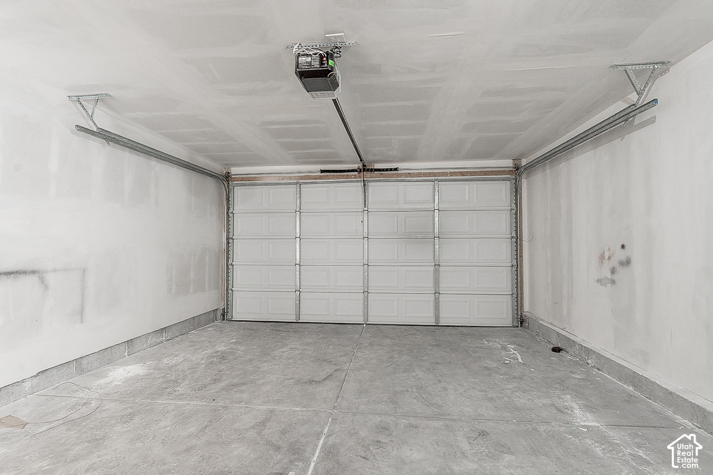 Spacious garage with a sectional overhead door, exposed ceiling joists, concrete flooring, and an automatic garage door opener mechanism