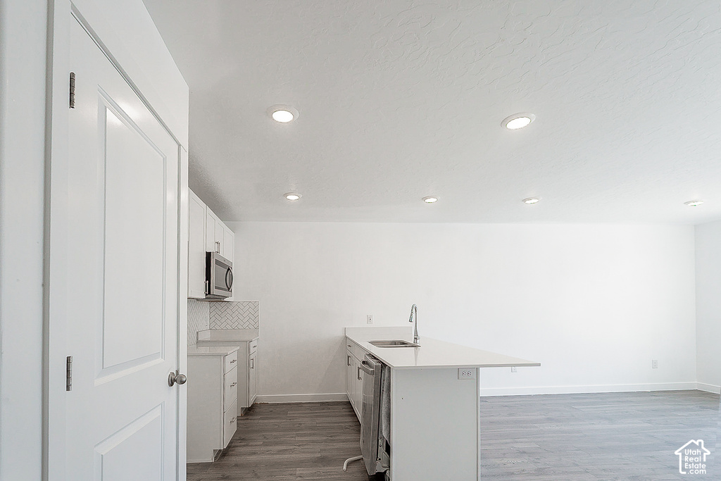 Contemporary kitchen featuring white cabinetry, stainless steel microwave, herringbone tile backsplash, and an island with an undermount sink