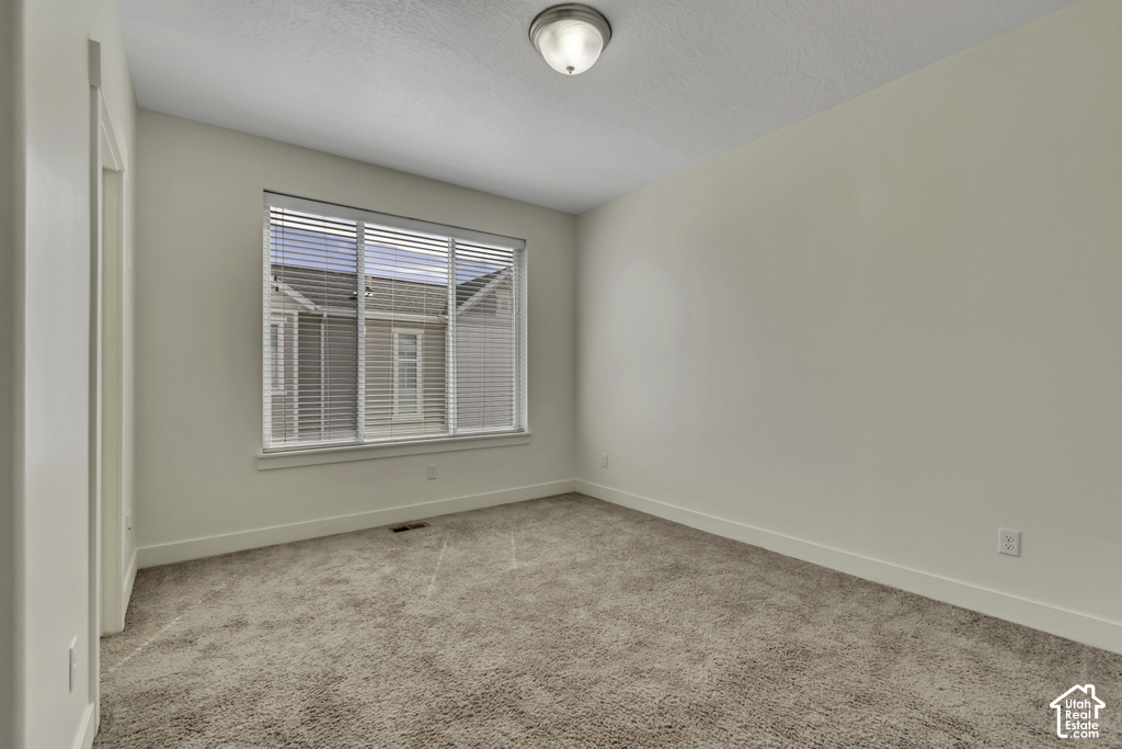 Spacious bedroom featuring neutral carpeting, large window with plantation shutters providing natural light, and clean white walls with recessed ceiling lighting