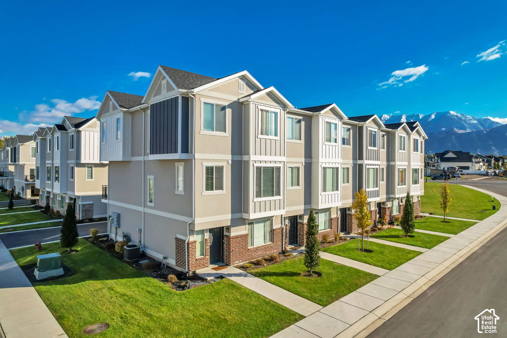 Modern townhome community featuring elegant exterior architecture with vertical and horizontal siding accents, multi-level design with peaked rooflines, and professionally landscaped grounds including manicured lawns, newly planted greenery, and concrete