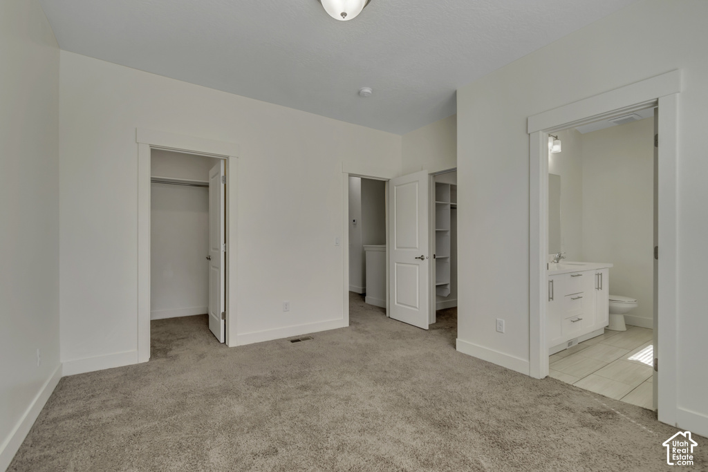 Carpeted room with white walls, featuring a closet with a white door, a laundry area with built-in shelving, and an en-suite bathroom with a white vanity and a toilet