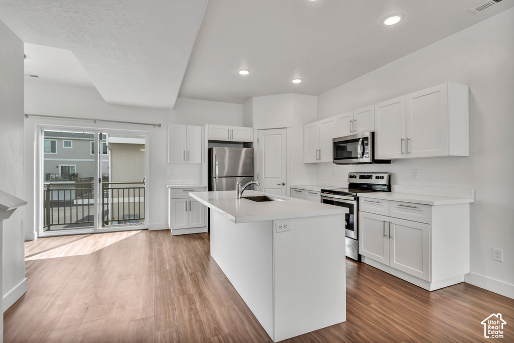 Contemporary kitchen featuring white cabinetry, stainless steel appliances, a center island with sink, quartz countertops, and wood-finish flooring