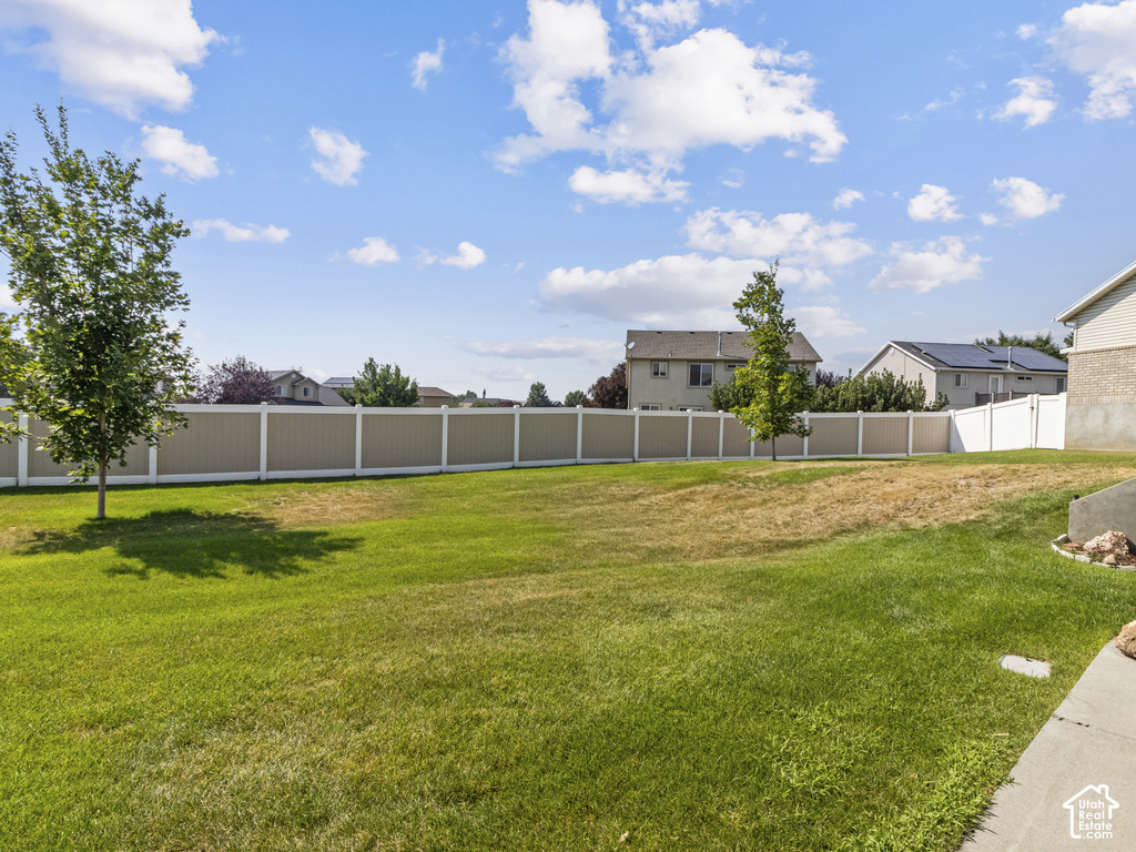 Expansive backyard with a combination of manicured lawn and dry grass, featuring a tan privacy fence with white posts, and young trees
