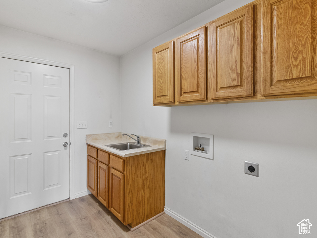 Laundry area featuring wood-finish flooring, a utility sink with a stainless steel faucet, a countertop, and built-in wood cabinetry