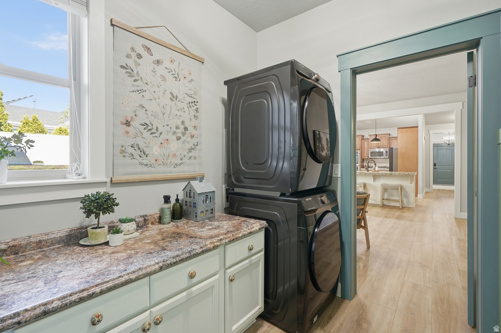 Dedicated laundry area featuring stacked appliances, a window providing natural light, a countertop with a decorative finish, and integrated cabinetry