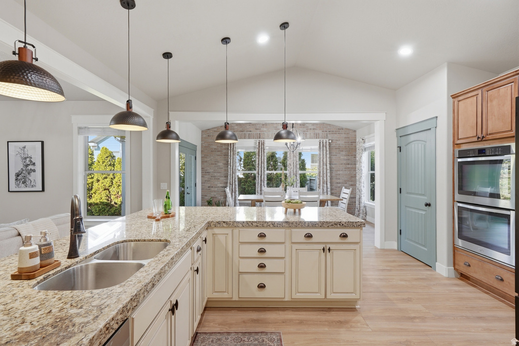 Spacious kitchen featuring a large island with a double basin sink, light-toned cabinetry, granite-style countertops, double wall ovens, and wood-finish flooring
