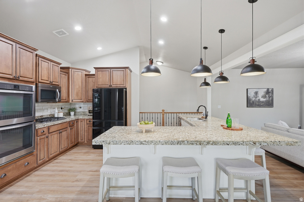 Kitchen featuring an expansive island with a light-toned countertop, pendant lighting, wood-finish flooring, wood cabinetry, and stainless steel double ovens