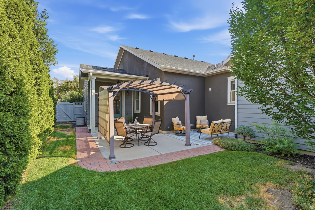 Expansive backyard featuring a concrete patio with pergola, brick paver accents, lush green lawn, mature perimeter landscaping, and privacy fencing