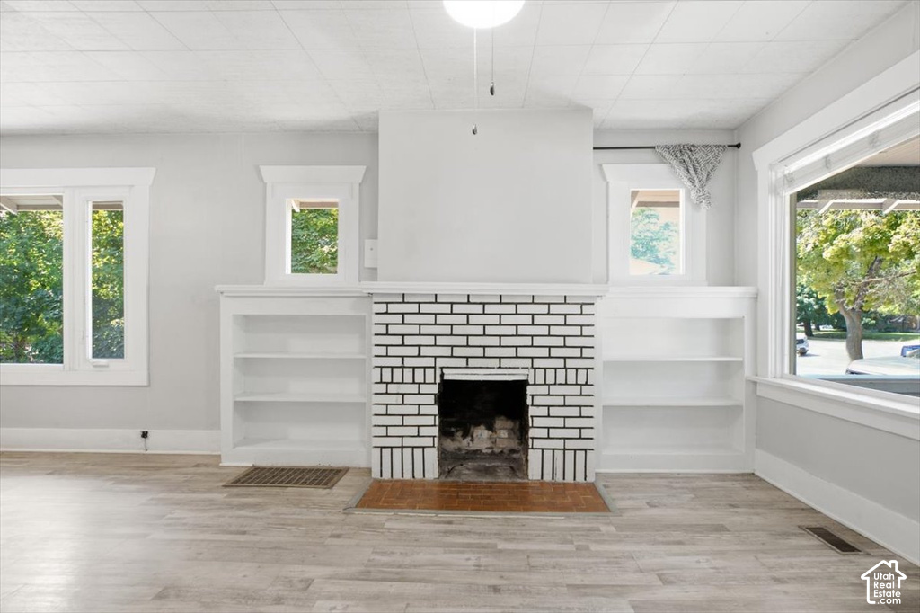 Built-in shelving, wood-finish flooring, white brick fireplace, multiple windows, ceiling light fixture