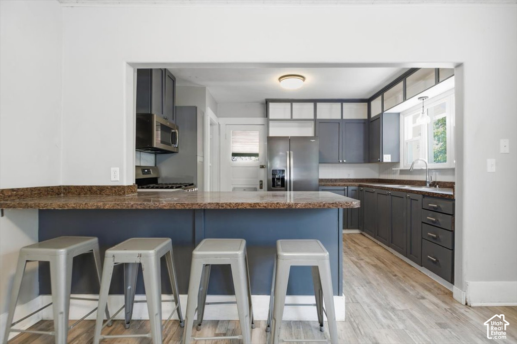 Kitchen featuring stainless steel appliances, wood-finish flooring, a breakfast bar, gray cabinetry, and a window over the sink