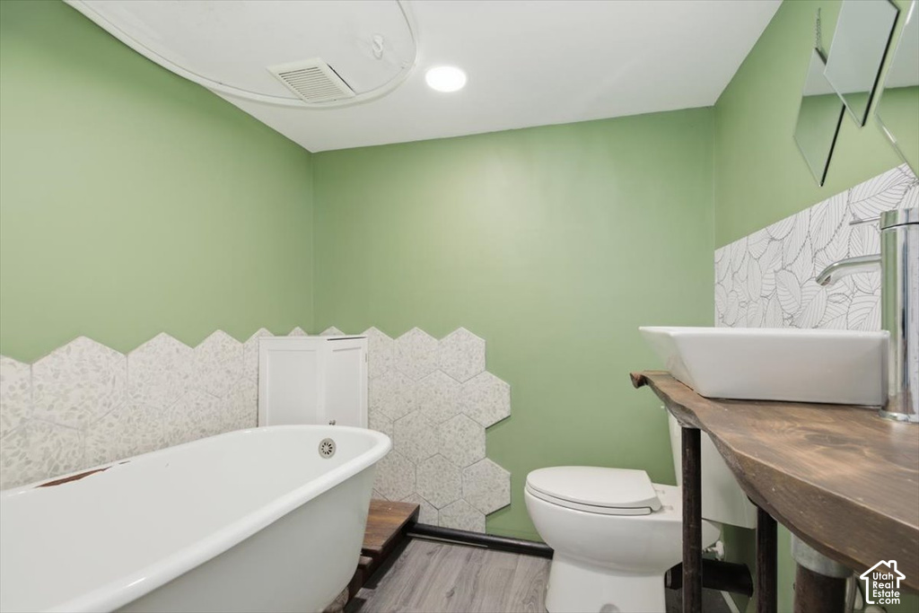Freestanding bathtub, wood-finish flooring, hexagon wall tile, white vessel sink, and a wood vanity