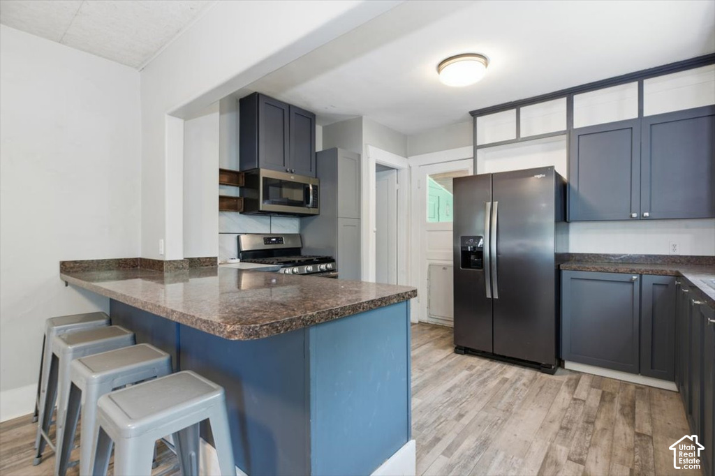 Kitchen featuring a built-in breakfast bar, wood-finish flooring, dark cabinetry, and stainless steel appliances