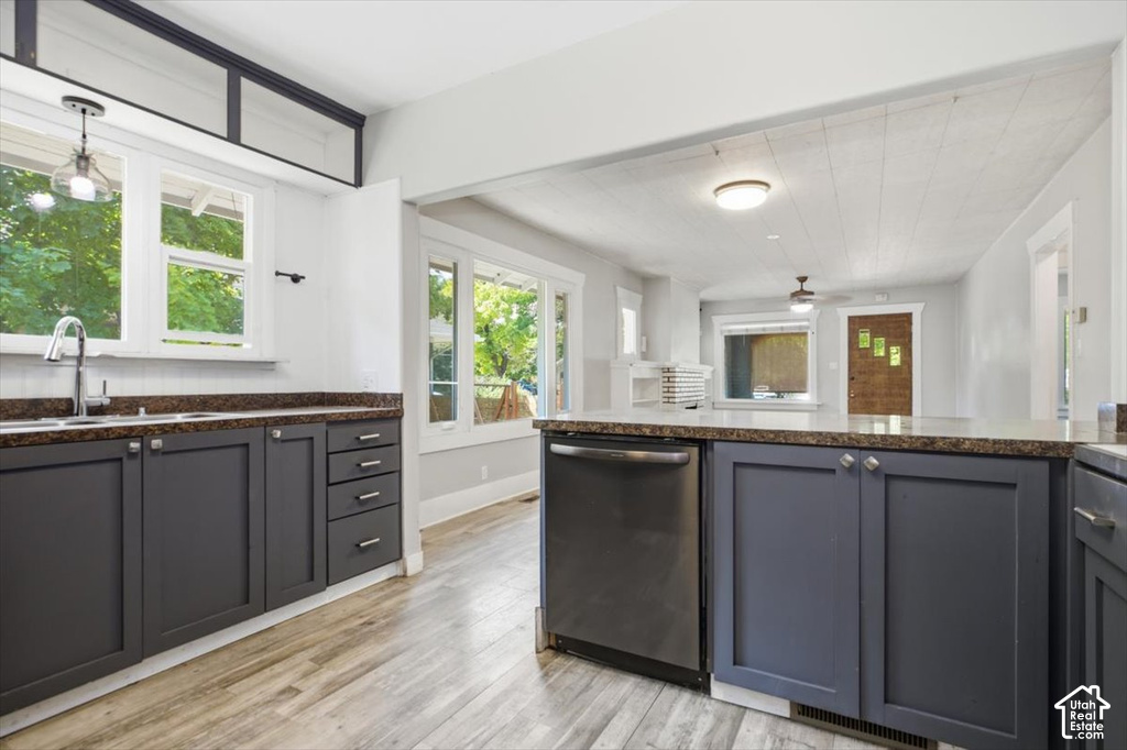 Modern kitchen featuring dark cabinetry with contrasting wood-finish flooring, stainless steel appliances including a built-in dishwasher, granite countertops, and abundant natural light from multiple windows and glass doors opening to outdoor space