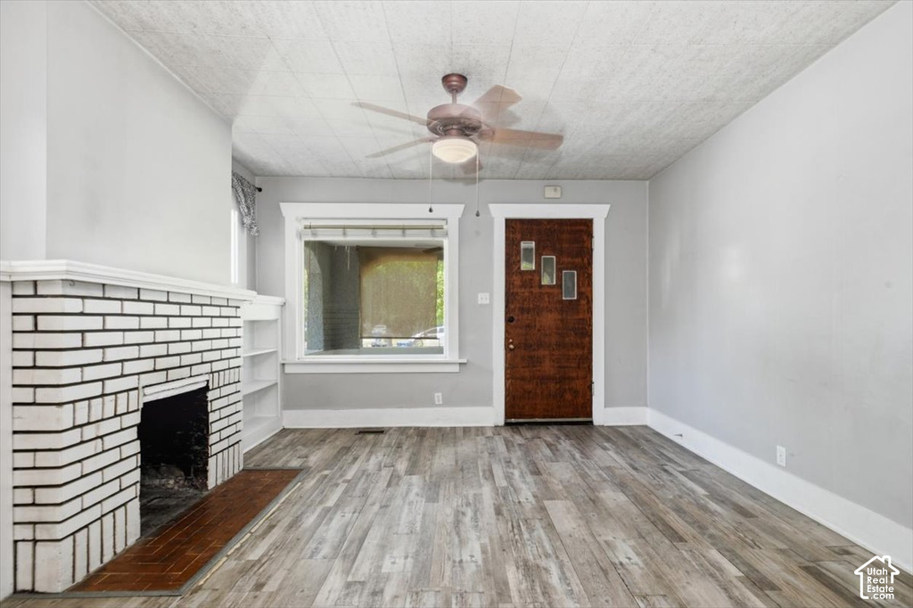 Bright living space featuring a wood-finish plank floor, white subway tile fireplace with dark hearth, ceiling fan with integrated lighting, and large window with white trim