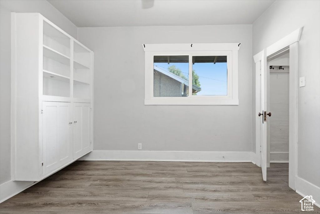 Bright and spacious room featuring hardwood-finish flooring, large dual-pane windows with natural light, custom white built-in cabinetry with shelving, and clean white walls throughout