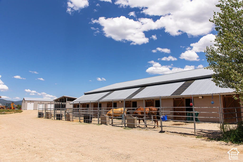 Barn structure with a metal roof and individual stalls, a separate outbuilding with a garage door, and a dirt lot