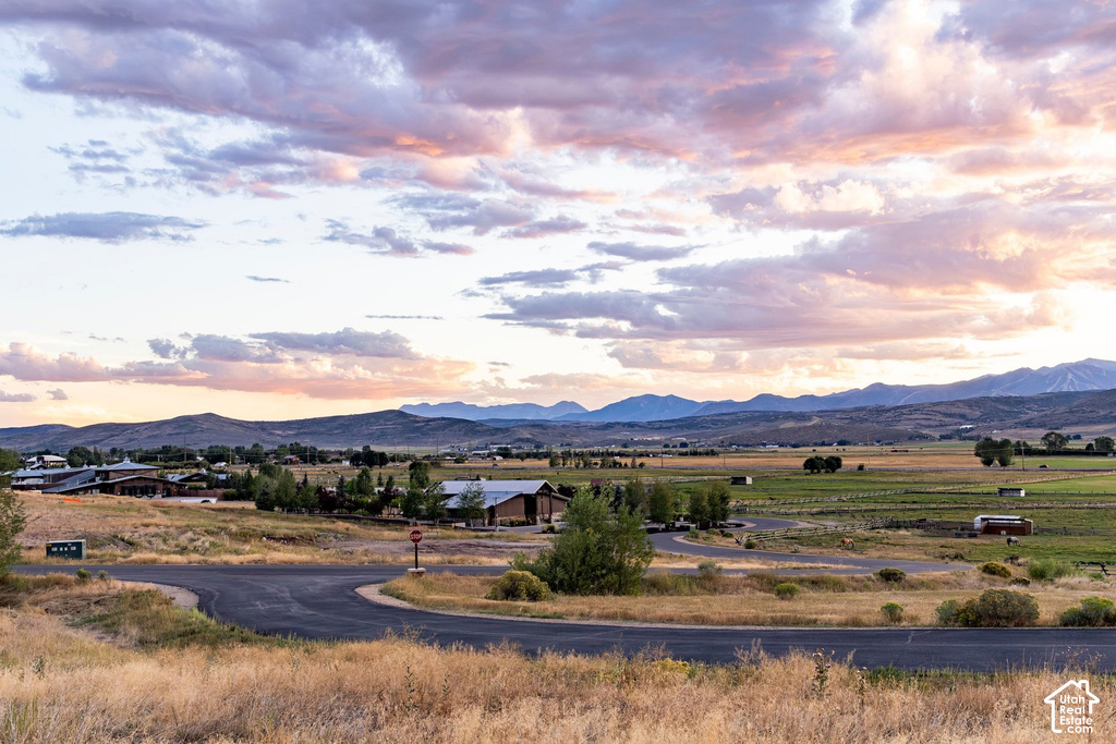 Expansive rural landscape featuring distant mountains, a meandering paved road, and scattered structures
