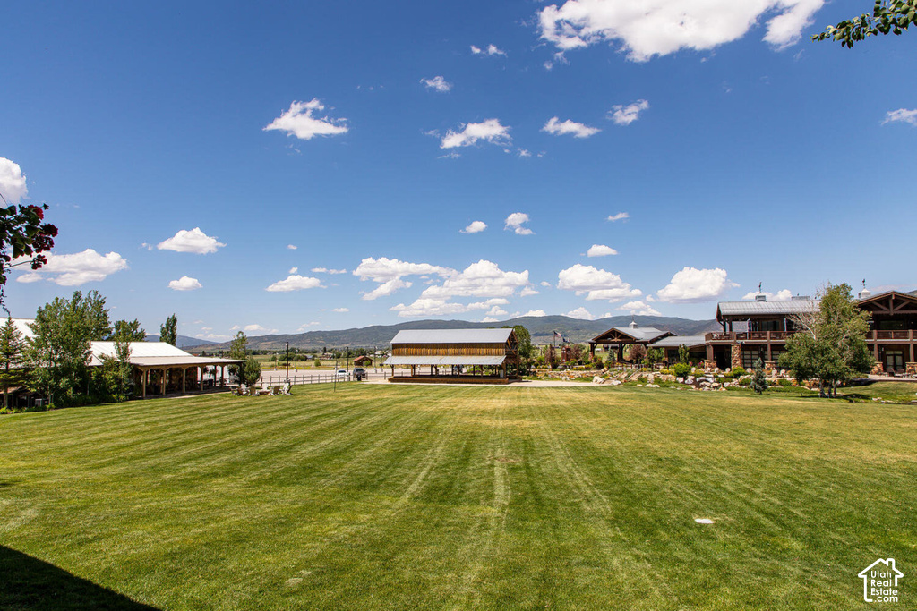 Expansive lawn with manicured grass, a rustic covered pavilion, a multi-level structure with stone facade, and a distant mountain range