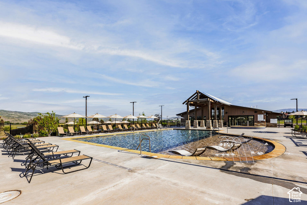 Outdoor swimming pool with integrated seating, adjacent lounge area with umbrellas, and an accompanying clubhouse with exposed beams